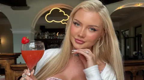 Blonde woman smiling at camera with a drink in her hand