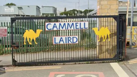 Cammell Laird gates, painted black with two yellow silhouettes of camels and the company's name in blue writing on a white background