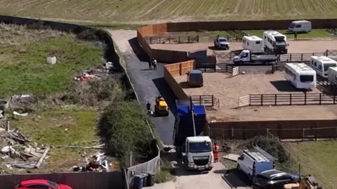 An aerial view of tarmac being laid next to a site with caravans on it.