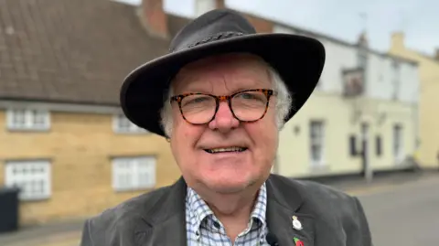 A head and shoulders photograph of Councillor Phil Dilks who is wearing a black hat, gray jacket and checked shirt