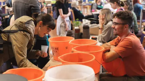 www.greenwoodland.photos Two people smile at each other over the top of a line of orange buckets at the BS3 Jammin event at St Paul's Church in Southville