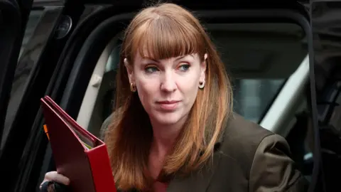 Reuters Angela Rayner, the Deputy Prime Minister, steps out of a vehicle in Downing Street wearing gold hoop earrings, and holding a red folder containing papers