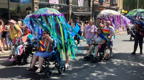 People in wheelchairs decorated in colourful ribbons celebrating Notts Pride in Nottingham city centre on 25 July.