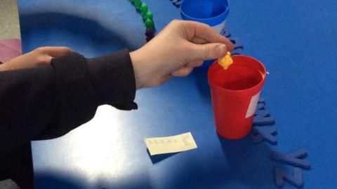 A child putting a small item into a red cup