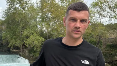 Arturs Juskins has short dark hair, is clean shaven and is wearing a black T-shirt with The North Face clothing brand logo in white lettering.