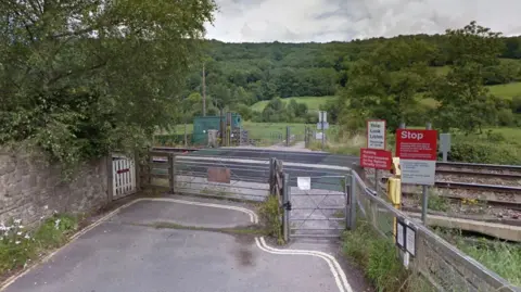 Google Google maps street view of a railway line near Warleigh Weir. There is a level crossing and a gate at its entrance as well as warning signs telling pedestrians to stop, look and listen out for trains.