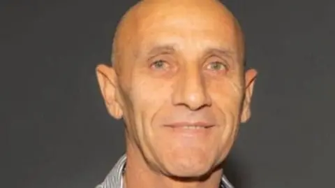 Yair Yaakov looking straight at the camera. He is bald and has grey eyes. He is wearing a striped shirt and smiling slightly.