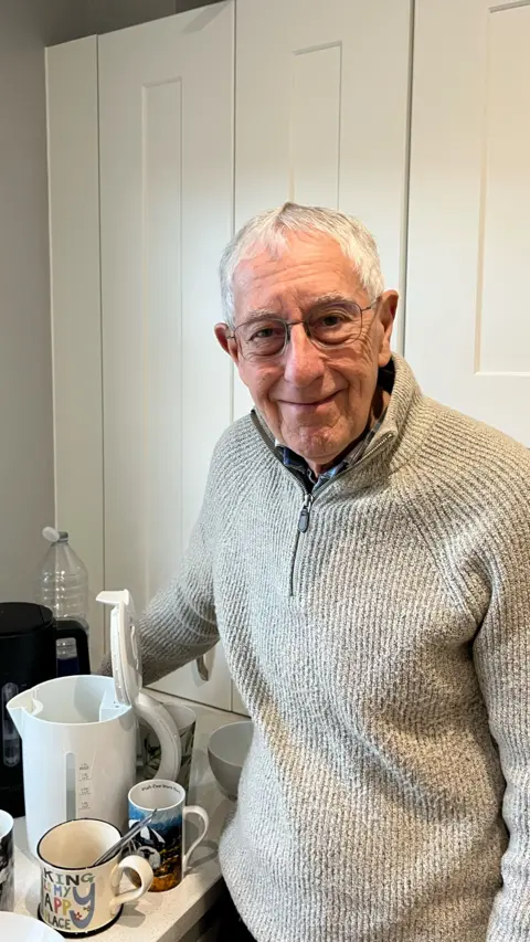 An elderly man in a grey cardigan.