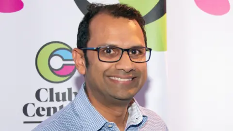 Club Central Head and shoulders shot of Panash Shah smiling, wearing a blue and white checked shirt.