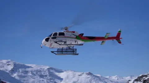 A helicopter is seen over snowy mountains