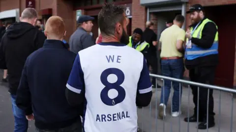 A Tottenham fan wearing shirt saying 'We 8 Arsenal'