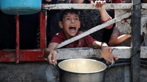 A Palestinian boy calls out while holding a pot waiting for food from a charity kitchen in Gaza City