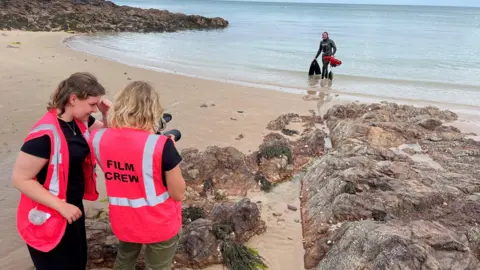 Two members of the film crew are shooting an image of the fisherwoman coming out of the sea