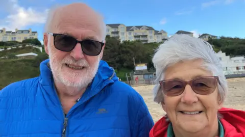 Man and woman wearing sunglasses and standing near the shore line on Carbis Bay Beach