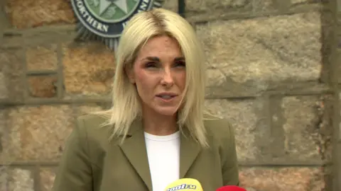 DCI Kerrie Foreman in white shirt and green blazer. She has blonde hair.