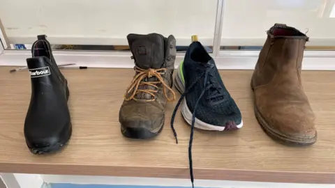 Barley Close Community Primary School Image of four left shoes including a short black wellington boot shoe, a brown walking boot, a black trainer and a brown suede Chelsea boot.