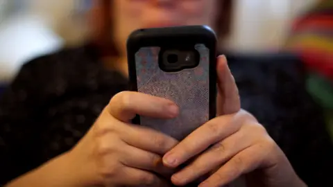 Stock image of a person on their phone. Their body and face is blurred but the back of their phone and hands are in focus.