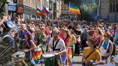 A sea of people with rainbow flags and brighly coloured clothing walking through Nottingham city centre. 