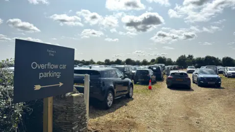 A huge number of cars in a field, with a dark sign for 