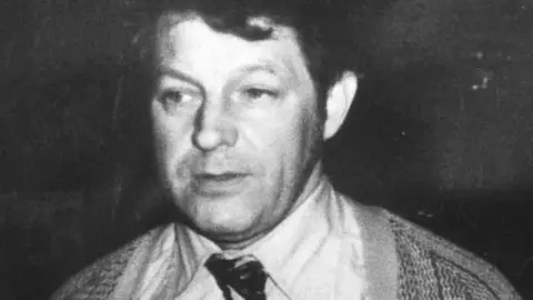 PA Media A black and white photo of a man with dark hair, wearing a shirt, tie and cardigan.