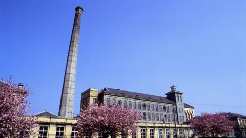 the exterior of Herdman's mill, a industrial looking mid 18th century building, now no longer in use. A huge chimney stack is seen to the left of a factory type building