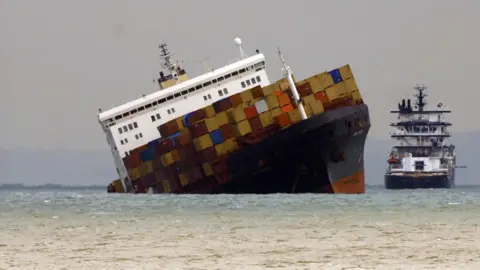 The Napoli lists heavily with containers on the deck and a tug off it's side