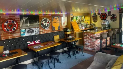 Tina Hibbs A photo of the inside of a garden shed pub. There is a bar and there are pub tables around. 