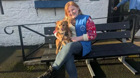 DGCR A woman with red hair sits with a golden small fluffy dog