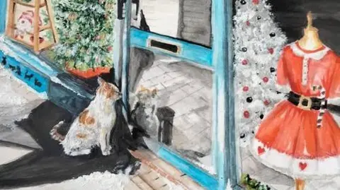Wendy Robinson Painting of a ginger and white cat sitting outside a shop door. In the background can be seen a shop window with a mannequin in the window wearing a red and white Christmas dress along with two Christmas trees and a shelf of china and ornaments.
