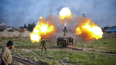 Getty Images Grassy terrain and three blasts in the sky coming from a weapon. A man is walking away from it, while another man - in the bottom left corner - is watching