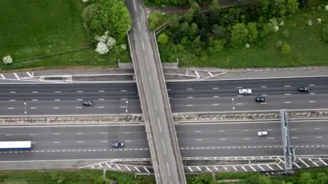 Getty Images A birds-eye view of a motorway. There is a bridge running across it. Trees/ a forest at the top of the image. 