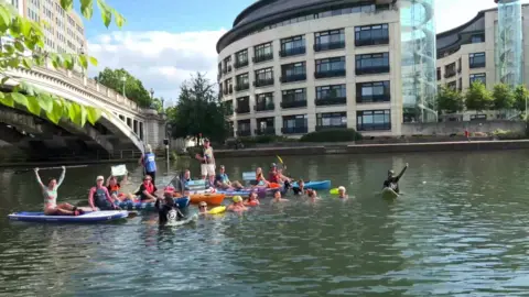 BBC Protesters floating on river thames some on paddle boards and some just bobbing in the water