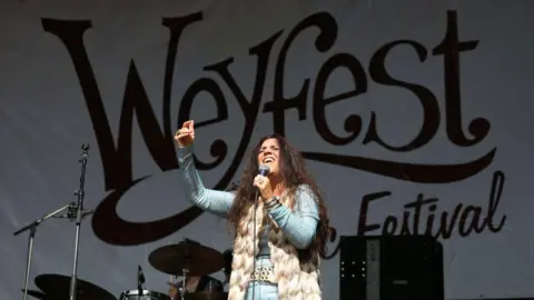 Sari Schorr performs on Day 2 of Weyfest Music Festival 2023 at the Rural Life Living Museum. A banner behind her on the stage reads Weyfest Festival