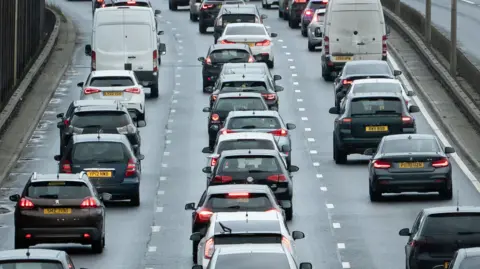 PA Media Three lanes of standstill traffic on a busy road on the A13 in England. A mix of cars and vans are on the road.