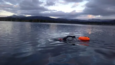 Supplied A woman swimming in a vast lake followed by her orange safety float