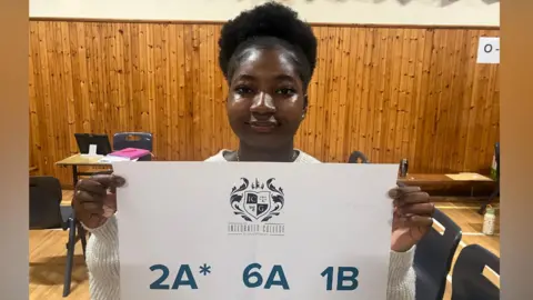 Girl with hair tied up holding sign with her results two A stars, 6six As and one B