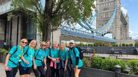 Collect/PA Real Life Mel (far left) with other warrior walkers at Tower Bridge. The ladies are wearing bright blue tops, with bright face paint on their cheeks, and all smiling at the camera.