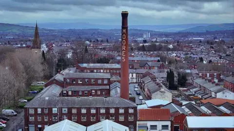 BBC An aerial view of the historic Moores Hat Factory and homes in Denton on February 18, 2026 in Manchester, United Kingdom