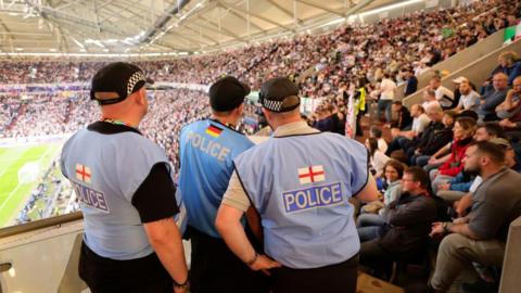 Police officers from England and Germany look towards a crowd inside a football stadium