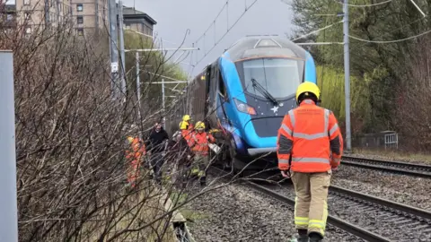 Jim Fleming A fireman walks back towards the dark blue train with five other firemen by the tracks 