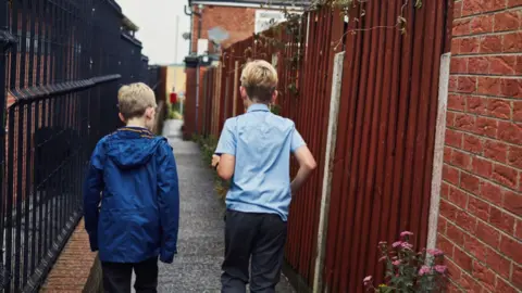 Two young boys walk down an alley way.