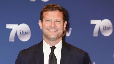 PA Media A man wearing a black suit and smiling at the camera