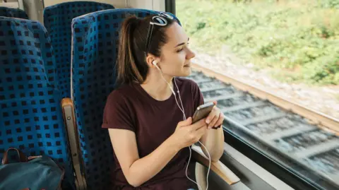 A teenage girl sitting on a train listening to headphones 