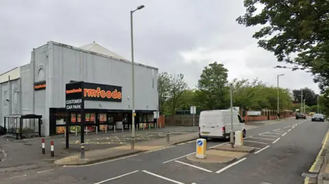 Streetview of where the crash happened. There is a road running alongside a large grey store with signage for Farmfoods written on it.