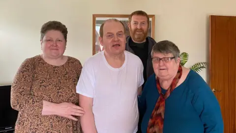 Andrew Quelch A family group photo of two men and two women standing together in a home.