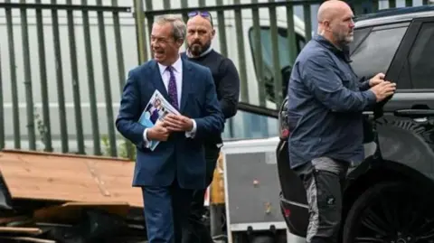 Getty Images Nigel Farage outside the Gurnos sports and social club before last year's UK general election. He is carrying Reform's policy pledges document. There are two other men nearby and a large black car Farage was using. Farage is wearing a blue suit, with a purple tie and holding a manifesto.