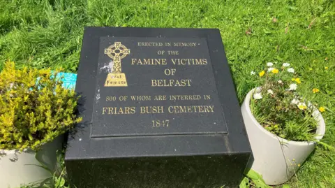 A black memorial stone set in grass. It reads 'Erected in memory of the famine victims of Belfast, 800 of whom are interred in Friars Bush Cemetery, 1847'. 