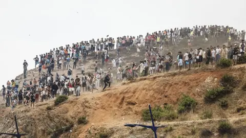 AFP via Getty Images Migrants attempting to cross into Spain's North African enclave of Ceuta gather on a hilltop during clashes with Moroccan security forces on July 31, 2026. 