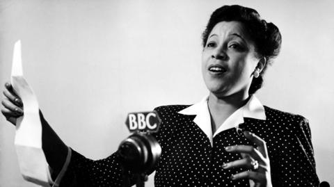 Adelaide Hall, shown black and white singing into a BBC microphone holding a white piece of paper in front of her