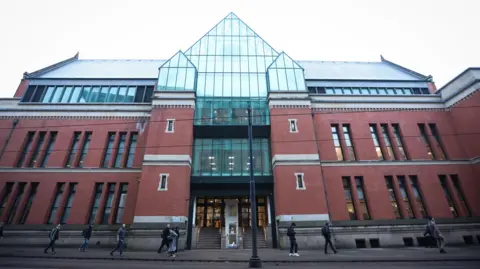 EPA The entrance to Minshull Street Crown Court in Manchester. with two sets of stairs in between two columns of the redbrick, multi-storey building, on top of which sits a wall of glass panels rising to a point. People can be seen walking along the pavement outside. 